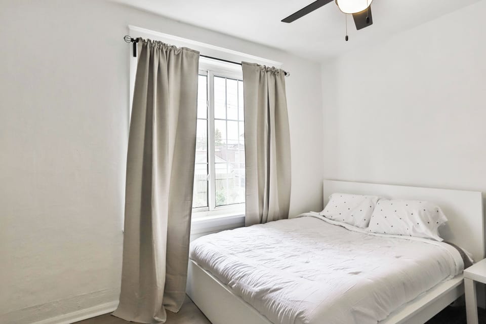 Bedroom 2 features a white bed, tall window with taupe curtains, ceiling fan, and nightstand.