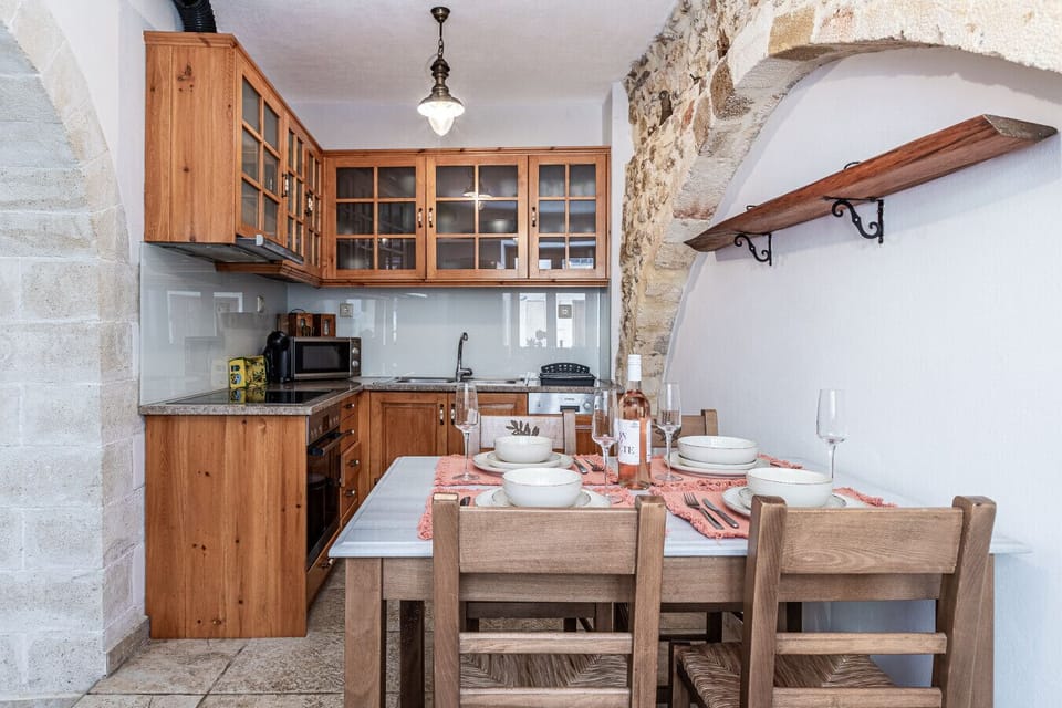 The kitchen of Casa Eleni features a fully equipped cooking space, a refrigerator, and a dining table with four seats, offering both functionality and comfort.