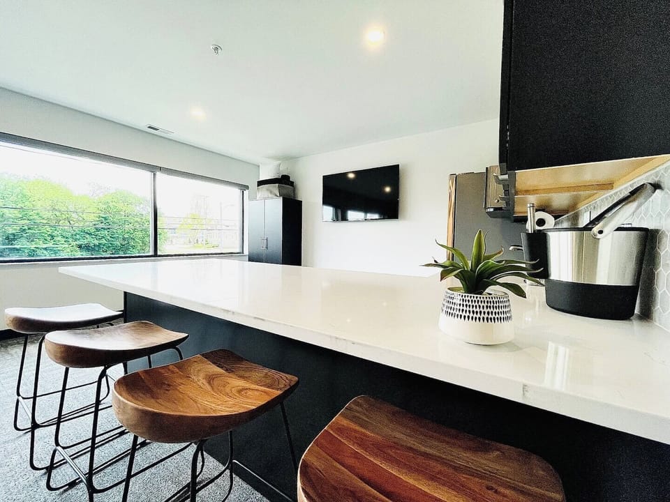 A sleek kitchen bar featuring stylish wooden stools and a mounted TV on the wall, creating a perfect spot to enjoy a meal or catch your favorite show while staying connected in the modern open-concept space.