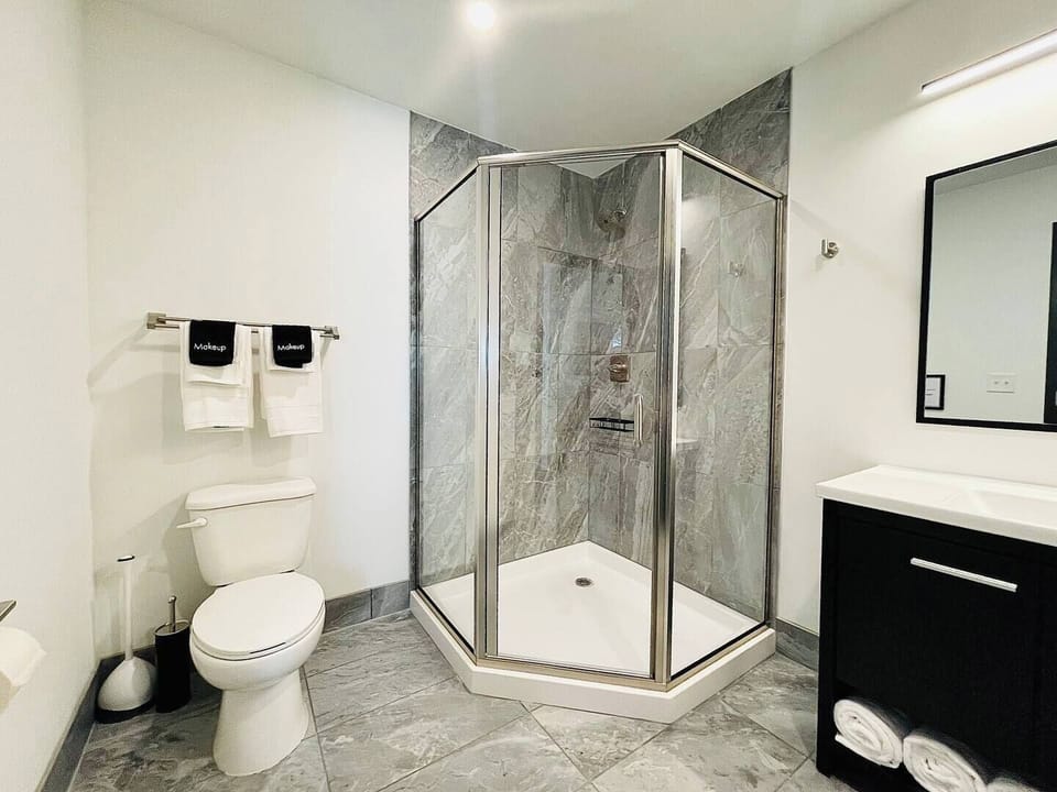  A pristine bathroom featuring a walk-in shower with elegant gray tiles, fresh towels, and modern amenities.