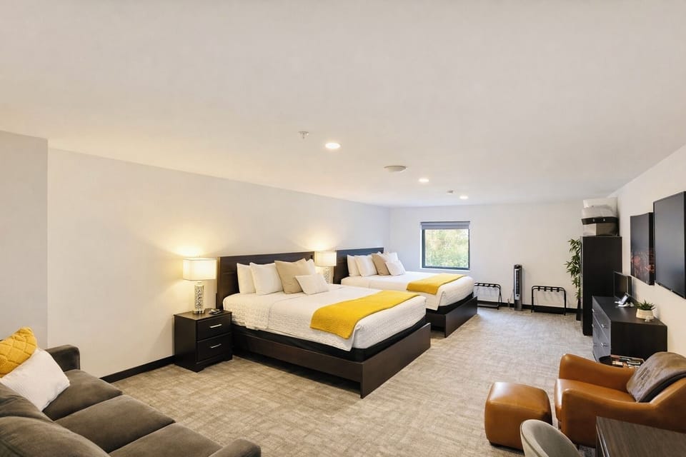 A bright, open room featuring queen beds, work desk, ample storage, and a large TV, perfect for relaxing or working during your stay.