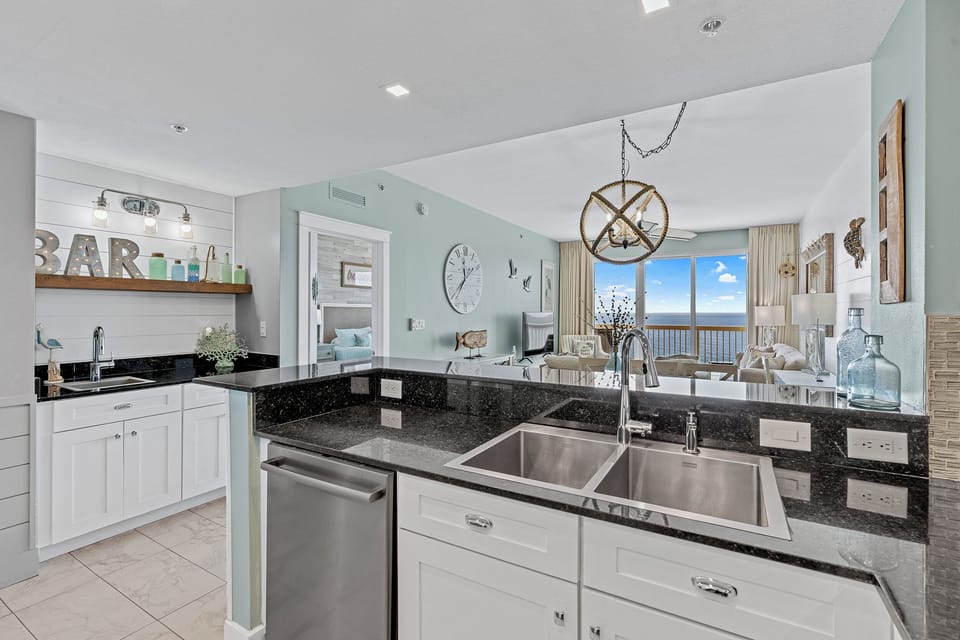 Your open-concept kitchen flows into a coastal-style living space with calming blue walls, stylish decor, and stunning ocean views through floor-to-ceiling windows.