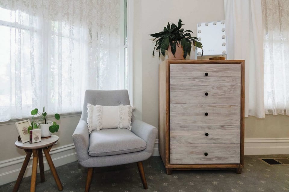 A cosy bedroom corner featuring a single armchair beside a small cabinet and a side table, providing a comfortable spot to relax while adding a touch of functionality and style to the space.