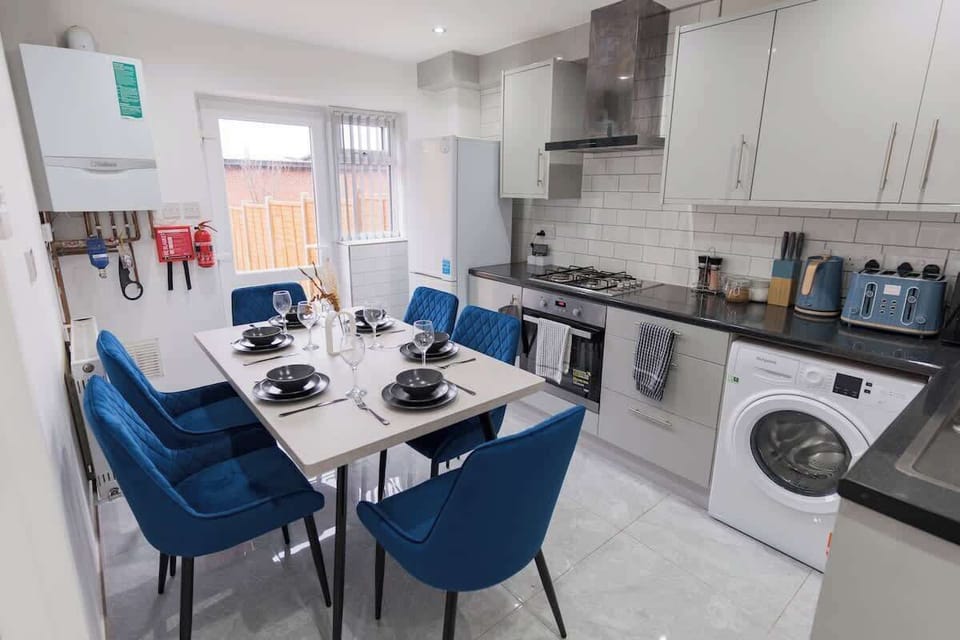 The bright, open-plan kitchen features glossy cabinetry and a six-seater dining table with striking sapphire-blue velvet chairs.