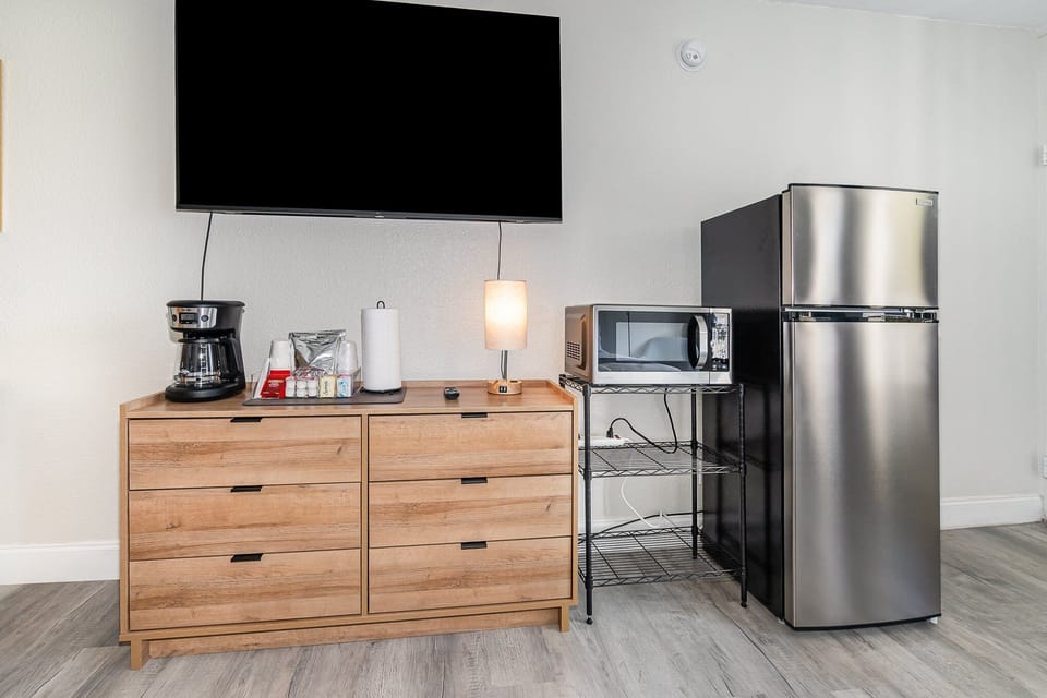 Enjoy the comforts of home with a sleek stainless steel refrigerator, microwave, and coffee station. A large smart TV and storage options complete this convenient and functional setup.