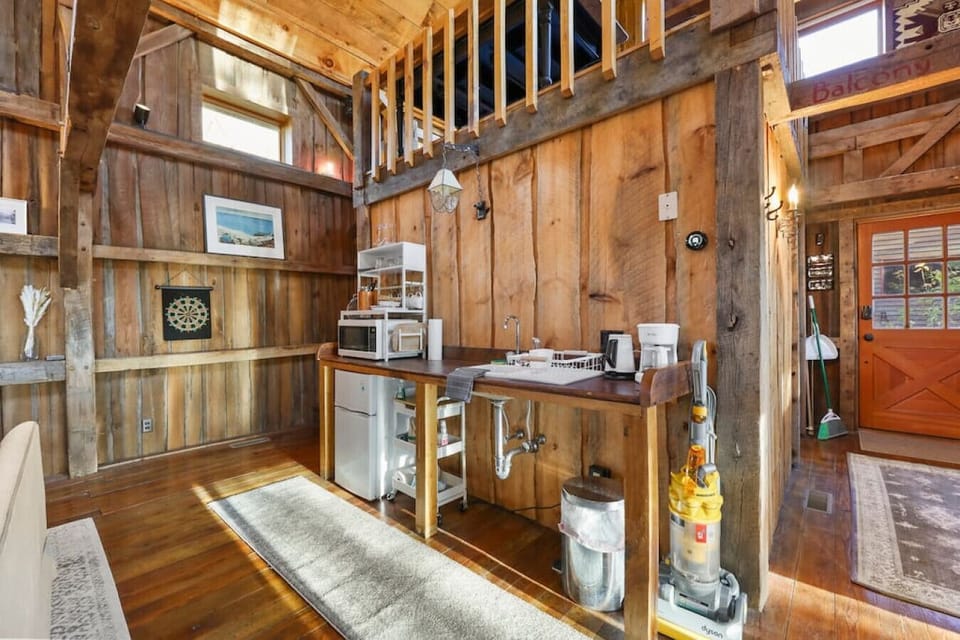 Functional kitchenette featuring a mini fridge, microwave, sink, coffee station, and shelving, all tucked into the corner of the open-plan living space.