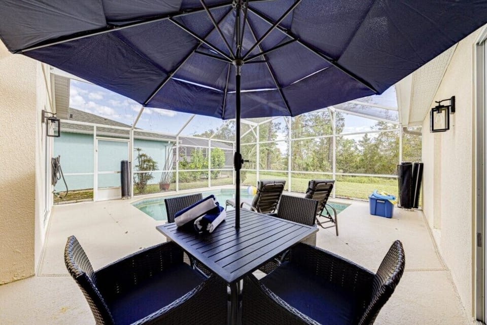 Poolside dining table with woven chairs and a large umbrella for shaded outdoor meals.