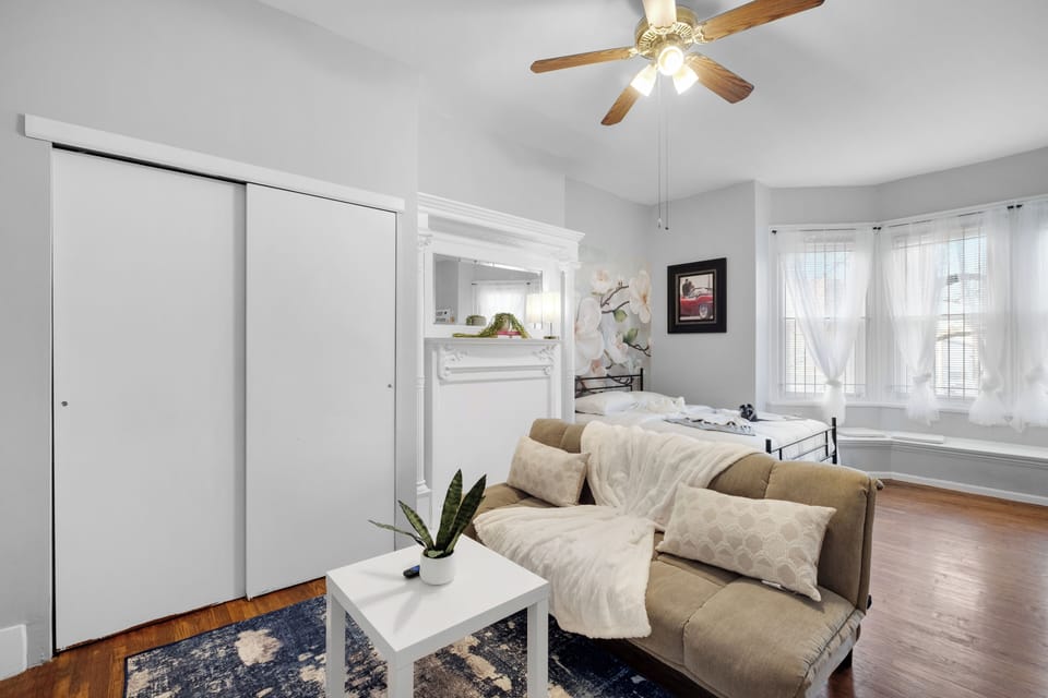 Bright, sun-filled studio with large bay windows and sheer curtains