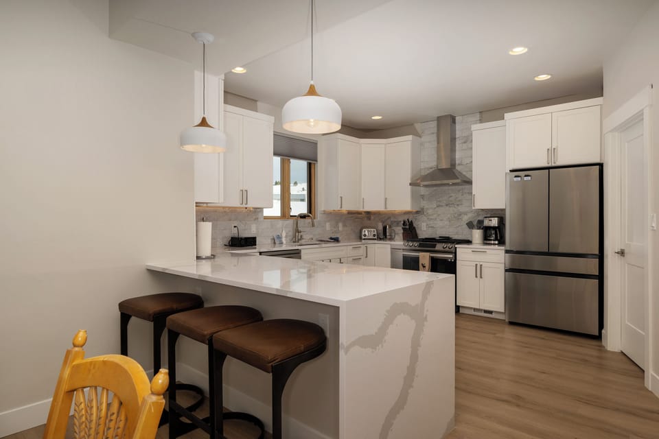 - Sleek, modern kitchen featuring a large island with bar seating for three - Stainless steel appliances and stone countertops add a touch of style - Pendant lights above the island create an inviting atmosphere for casual meals