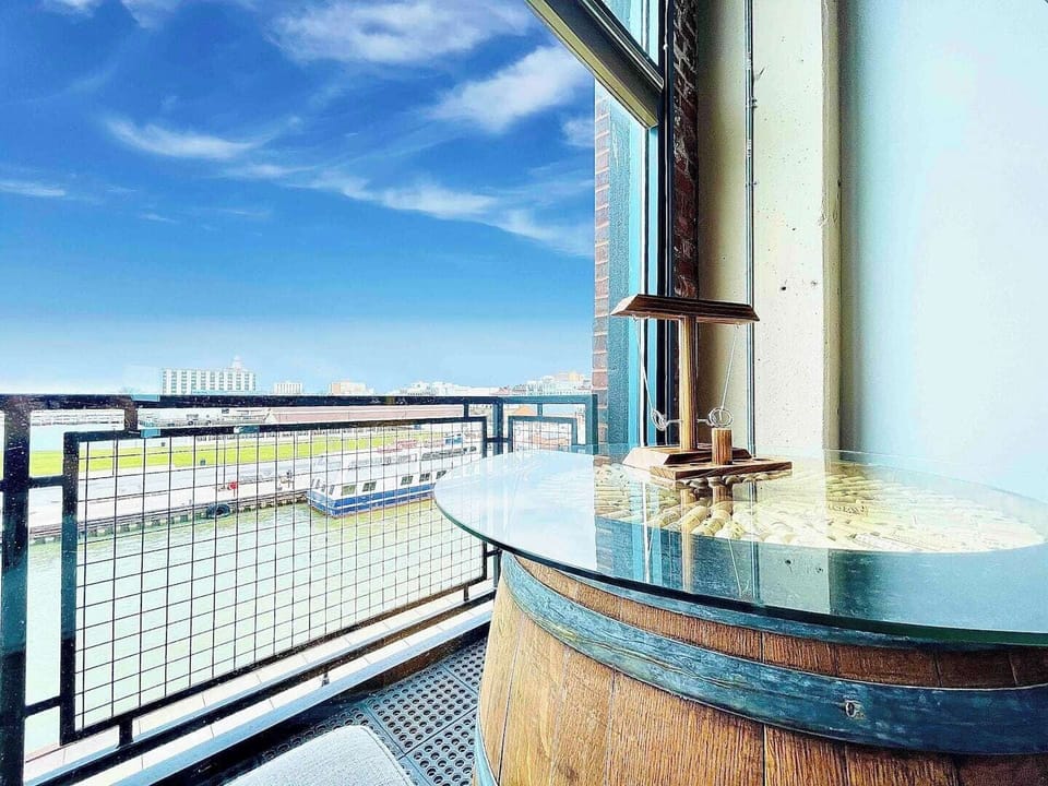 A unique barrel-style table overlooking the waterfront, offering serene views of the marina and surrounding cityscape under a bright blue sky.