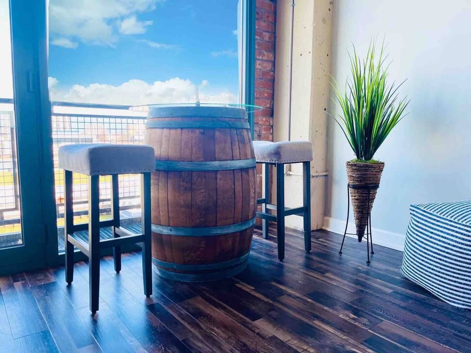 A unique and rustic bar table crafted from a barrel, paired with upholstered stools. Situated by the floor-to-ceiling windows, offering scenic views and a cozy spot for drinks or conversation.

