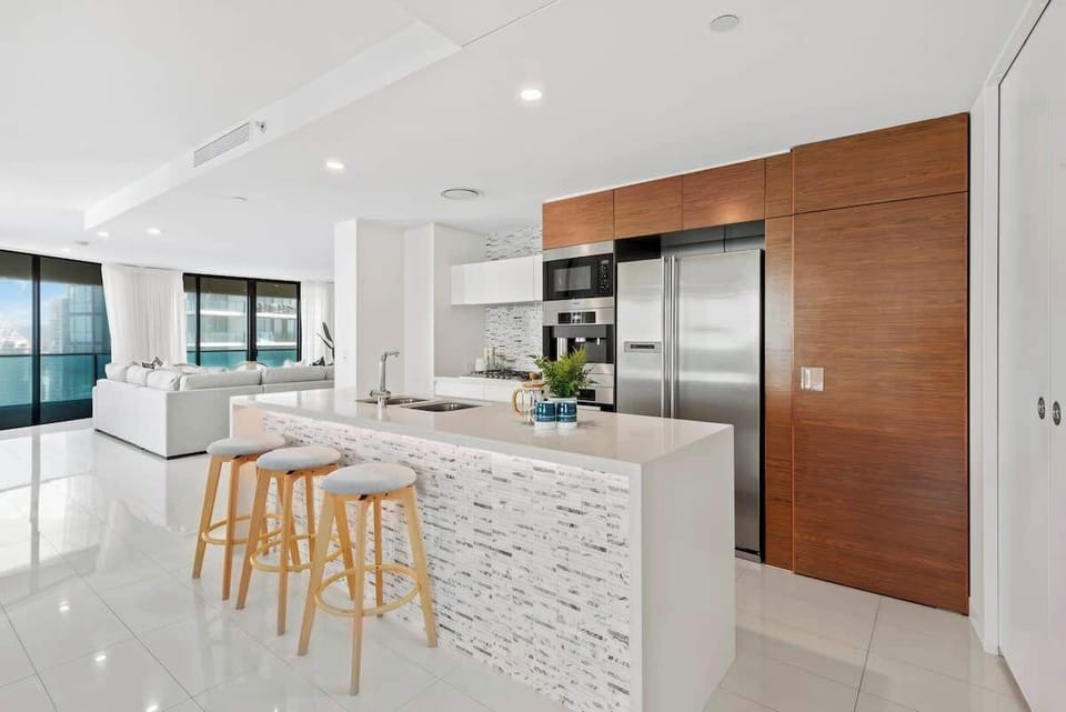 Modern kitchen with stainless steel appliances, large fridge, & an island bench.