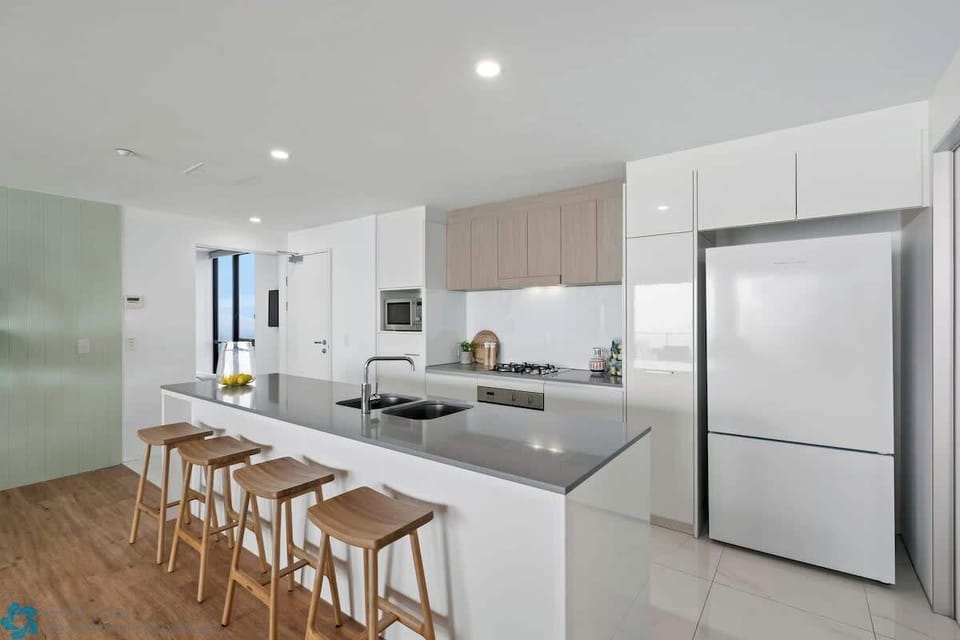 Modern kitchen with stainless steel appliances, large fridge, & an island bench.
