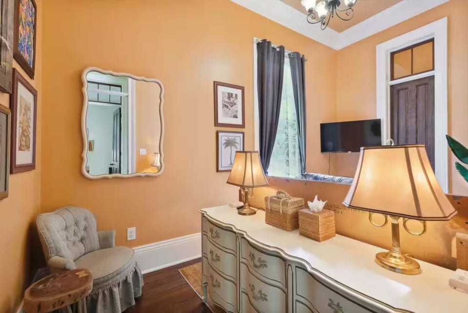 Bedroom 1 features a comfortable queen-size bed with layered pillows and soft bedding, accented by tall windows and eclectic artwork.