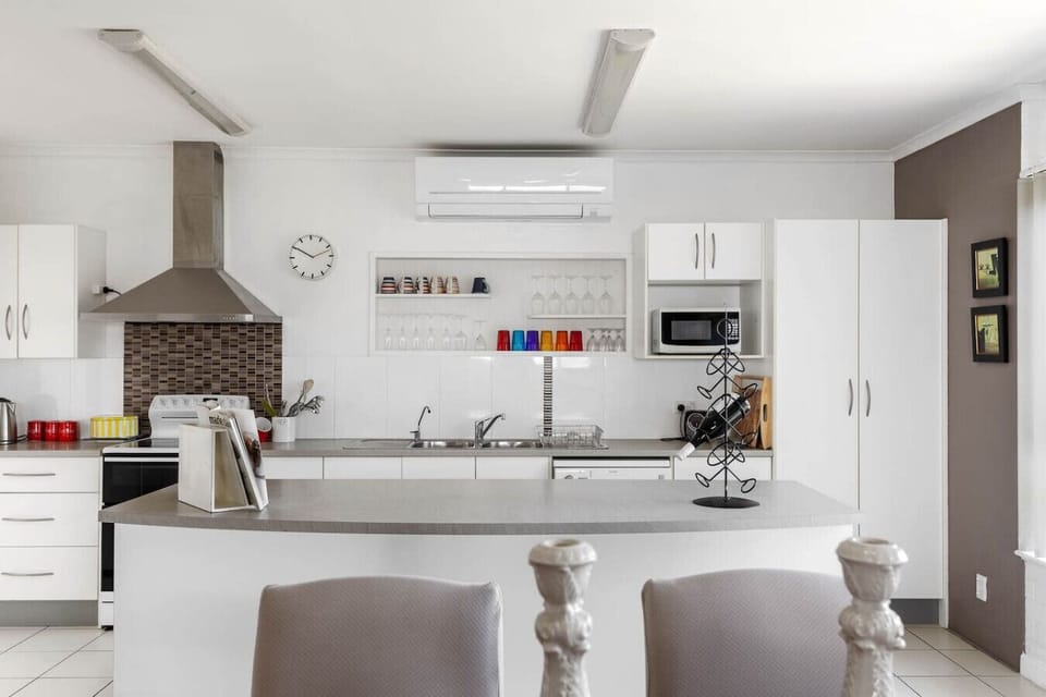 The kitchen features a stainless steel range hood, a microwave, and a wine rack on the island. There are also colorful glassware on a shelf and a clock on the wall, contributing to a stylish and organized look.