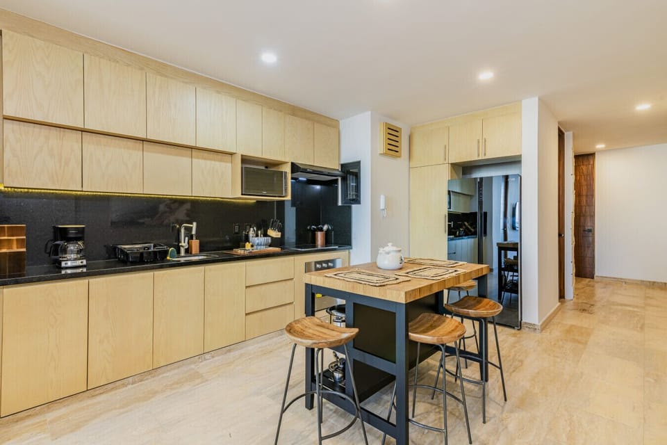 Cocina moderna y totalmente equipada con acabados en madera, barra desayunadora y todo lo necesario para preparar tus comidas con comodidad durante tu estancia.