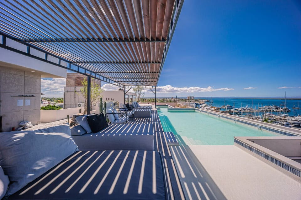 Terraza rooftop con alberca y espectaculares vistas al mar y la marina. Un espacio ideal para relajarte, disfrutar el sol y descansar en cómodos lounge chairs bajo una elegante pérgola.