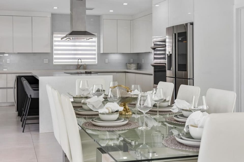 Sophisticated dining area with premium glass furnishings and sleek modern kitchen backdrop