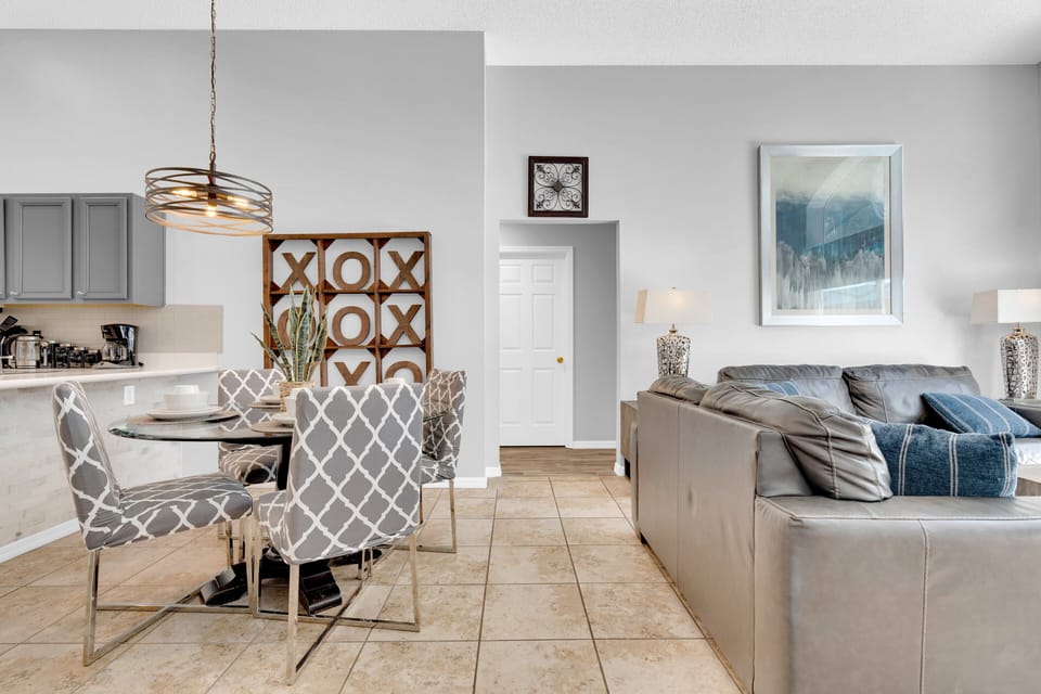 Modern dining space at Seasons near Disney includes glass table, printed chairs, and open access to the kitchen and living room.