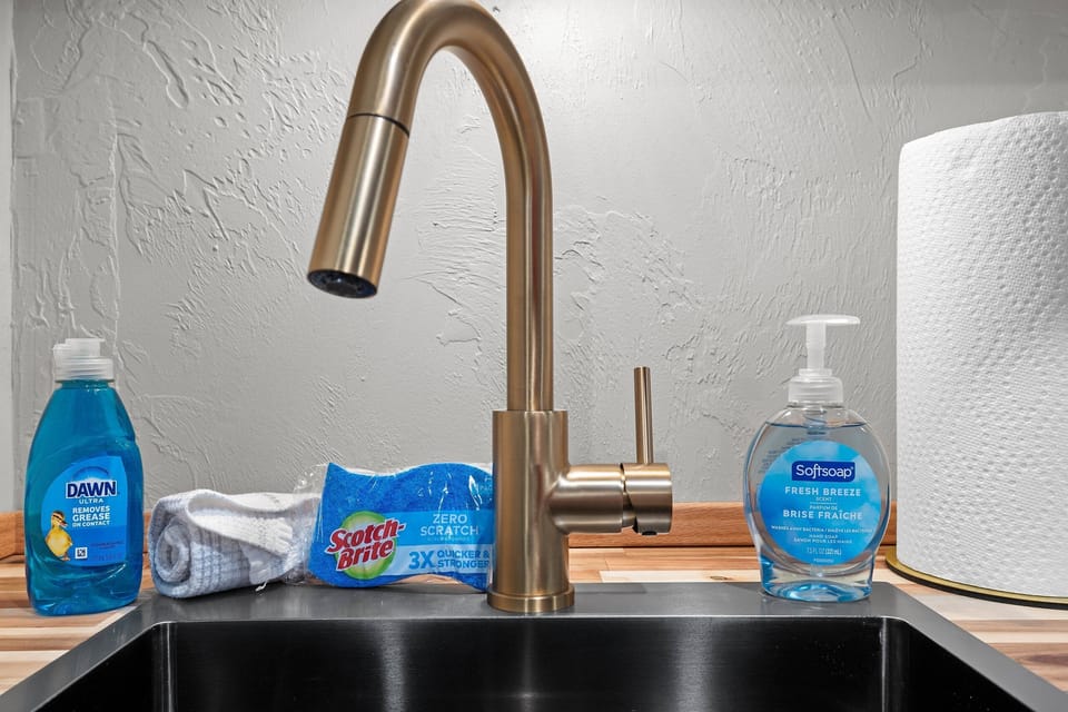 Modern kitchen sink with stylish gold faucet and essential cleaning supplies