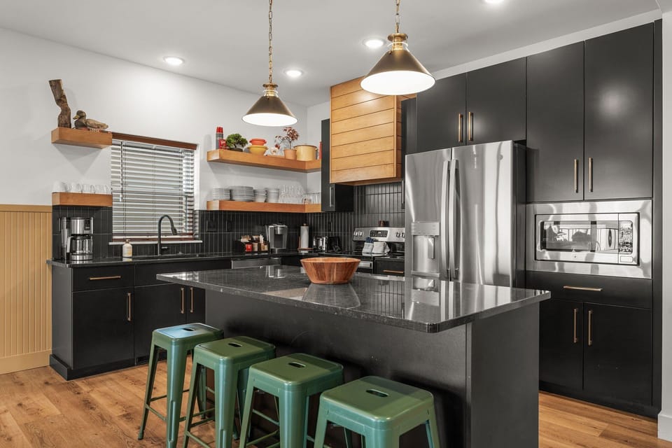 - Cook up a storm in this sleek, fully equipped kitchen with stainless steel appliances
- Open shelving, warm wood accents, and dramatic black cabinetry offer rustic modern charm
- Grab a seat at the island for breakfast, coffee, or conversation