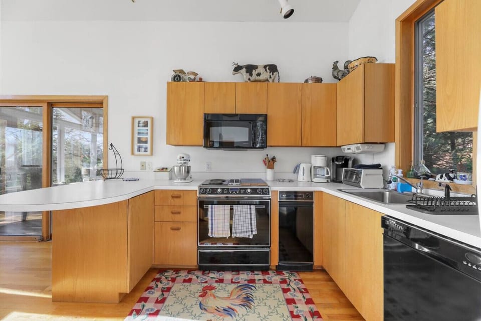 Bright kitchen with warm wooden cabinetry, a full range stove, microwave, coffee maker, stand mixer, and dishwasher, plus scenic window views.