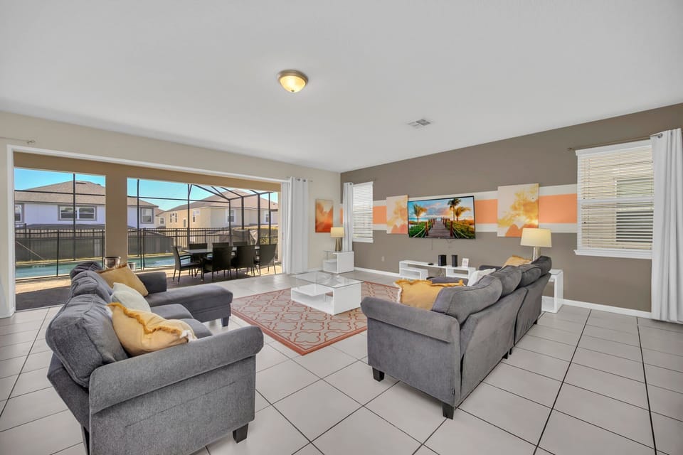 Bright and inviting living room with plush seating, a large flat-screen TV, and stylish decor. The open layout seamlessly connects to the dining area and extends to the screened patio and pool, perfect for relaxation and entertainment.