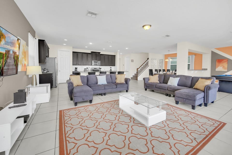 Bright and inviting living room with plush seating, a large flat-screen TV, and stylish decor. The open layout seamlessly connects to the dining area and extends to the screened patio and pool, perfect for relaxation and entertainment.