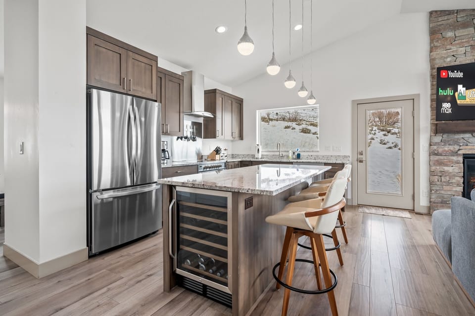 The gourmet kitchen features an island with seating for three and is equipped with stainless steel appliances, including a microwave, electric stove, and spacious refrigerator.