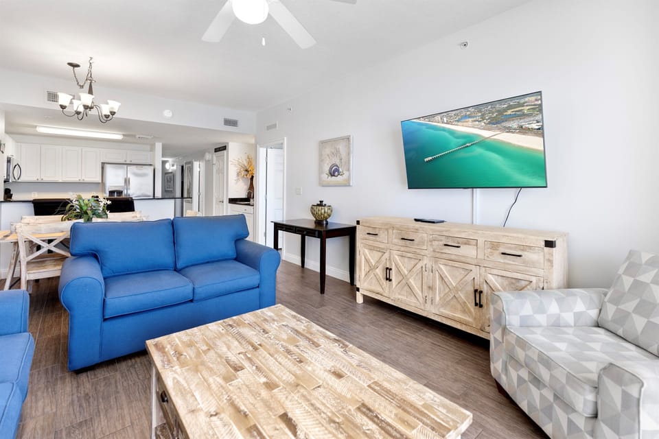 Relax in your bright, coastal-inspired living space featuring a comfortable blue sofa and entertainment center for perfect evenings in.