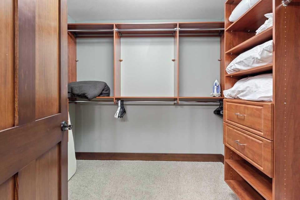 Primary bedroom walk in closet with iron and ironing board.