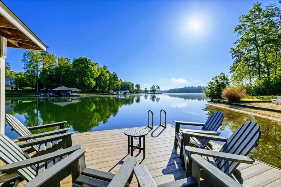 A peaceful end-of-dock seating area with Adirondack chairs, a swim ladder, and panoramic views of the still cove and surrounding tree line.