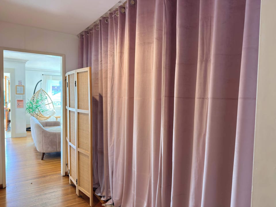 Maximize your space and privacy with these floor-to-ceiling blackout curtains and a classic rattan folding screen, perfect for creating a secluded nook or partitioning the room for extra guests.
