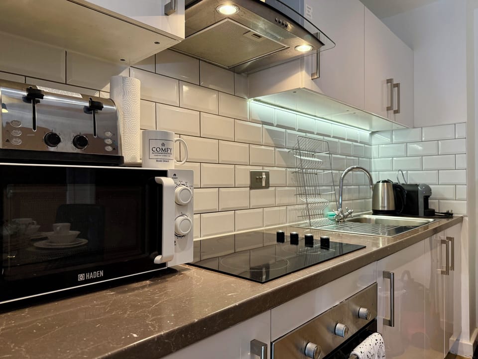 Modern compact kitchen with a sleek hob, oven, microwave, and kettle. Perfect for self-catering stays.