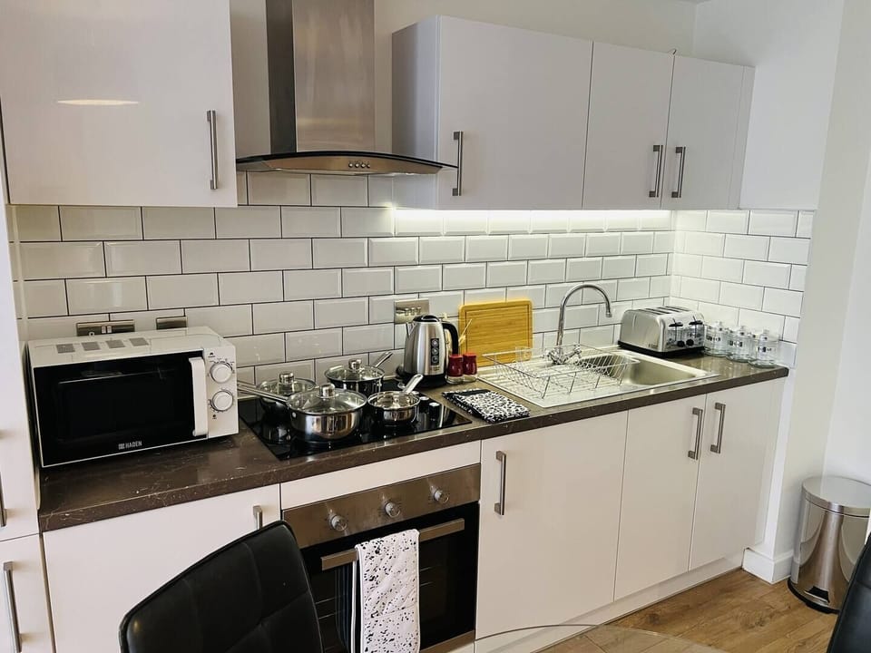 A modern, fully equipped kitchen with sleek white cabinetry, a gas stove, microwave, toaster, and kettle—perfect for home-cooked meals