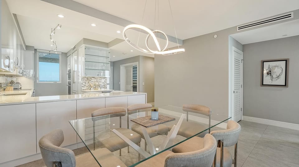 Glass dining table with beige fabric chairs sits beneath a contemporary triple-loop LED chandelier in the dining area.