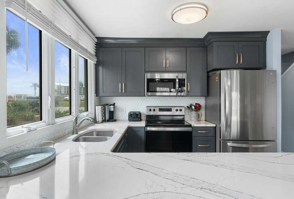 Stylish kitchen with quartz countertops, stainless steel appliances, and navy cabinetry—enjoy cooking with a view through the bright corner window.