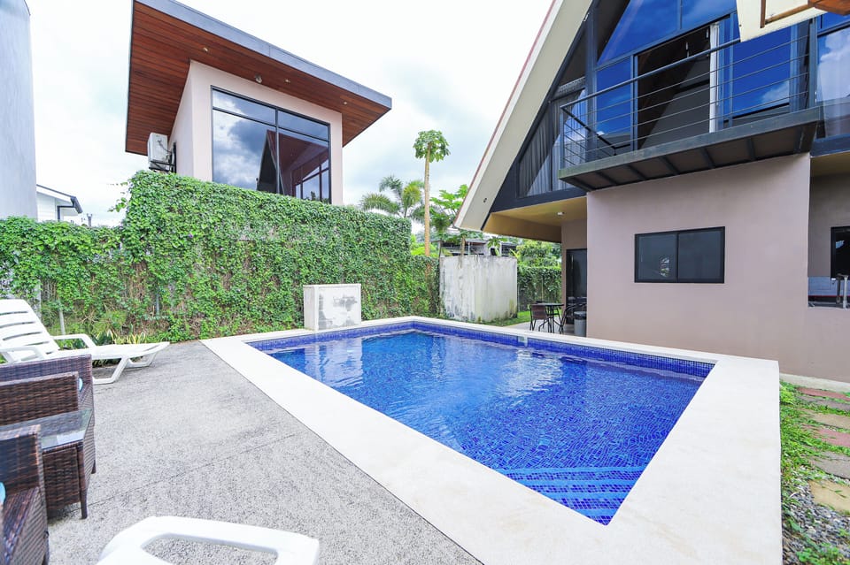 Swimming pool, loungers and the house exterior beside the garden hedge.