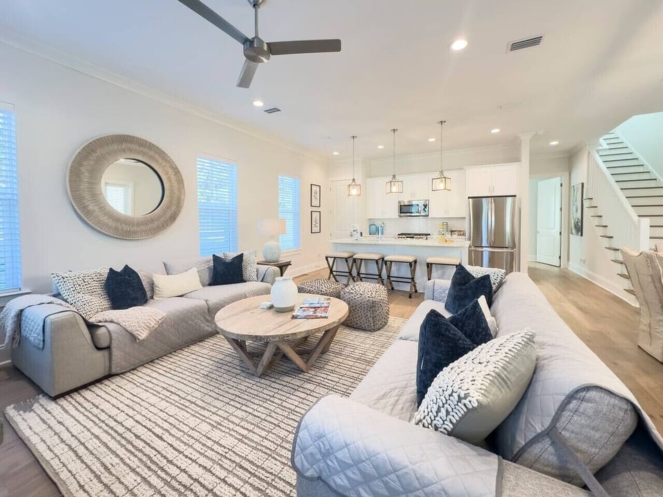 Bright open living area with deep couches, a relaxed coastal aesthetic, and seamless sight lines into the kitchen.