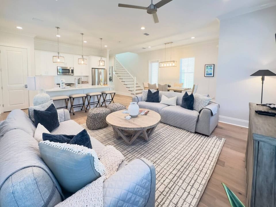 Bright open living area with deep couches, a relaxed coastal aesthetic, and seamless sight lines into the kitchen.