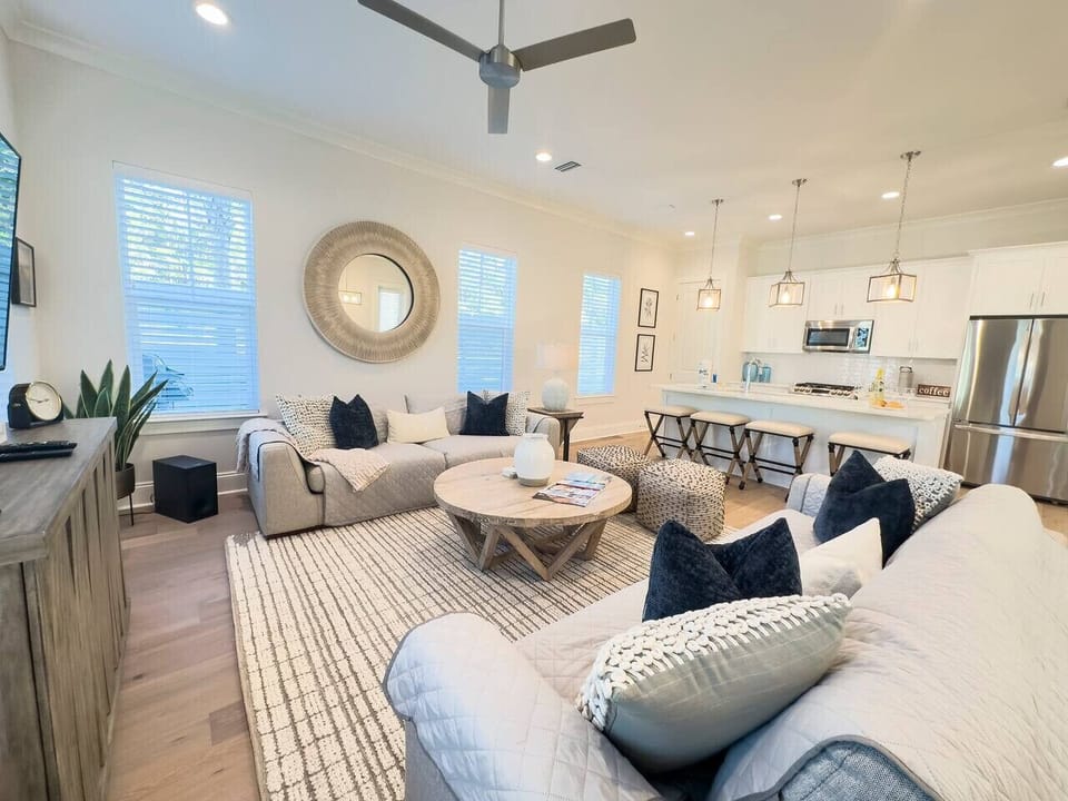 Bright open living area with deep couches, a relaxed coastal aesthetic, and seamless sight lines into the kitchen.