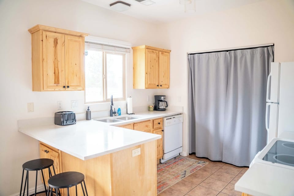 Fully equipped kitchen with wood cabinets, white counters, and cozy breakfast bar seating at Kanab Pad F4.