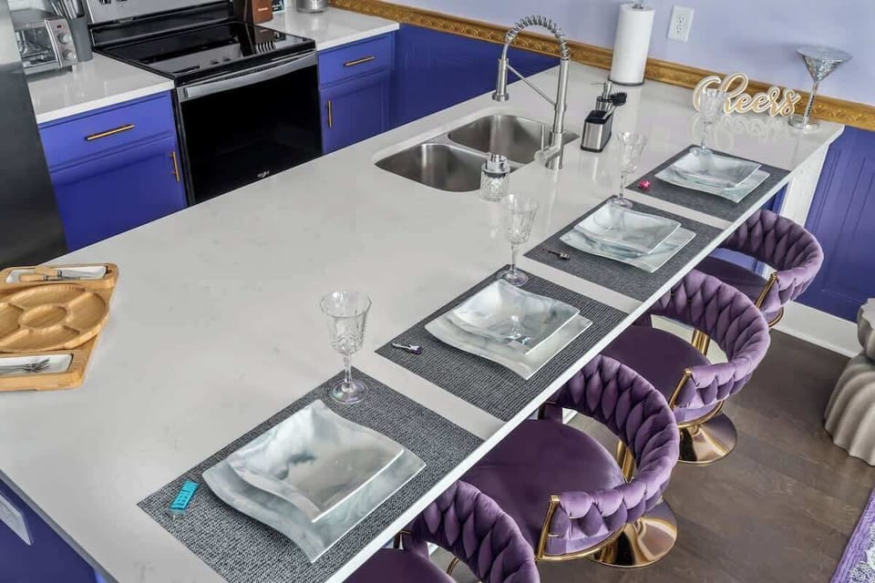 Whip up glam meals in this bold purple kitchen featuring luxe velvet barstools, stainless steel appliances, and sparkling accents. Perfect for entertaining in style or enjoying a cozy coffee moment at the chic breakfast bar.