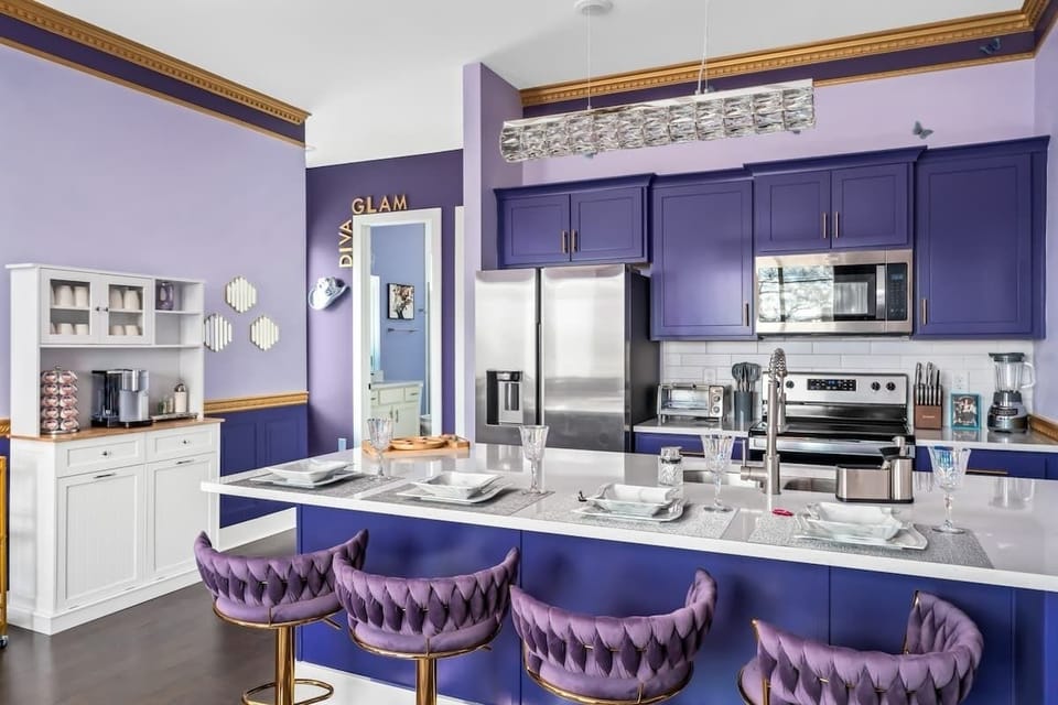 Whip up glam meals in this bold purple kitchen featuring luxe velvet barstools, stainless steel appliances, and sparkling accents. Perfect for entertaining in style or enjoying a cozy coffee moment at the chic breakfast bar.