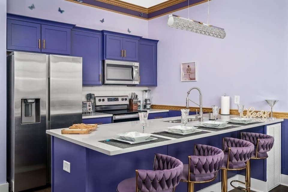 Whip up glam meals in this bold purple kitchen featuring luxe velvet barstools, stainless steel appliances, and sparkling accents. Perfect for entertaining in style or enjoying a cozy coffee moment at the chic breakfast bar.