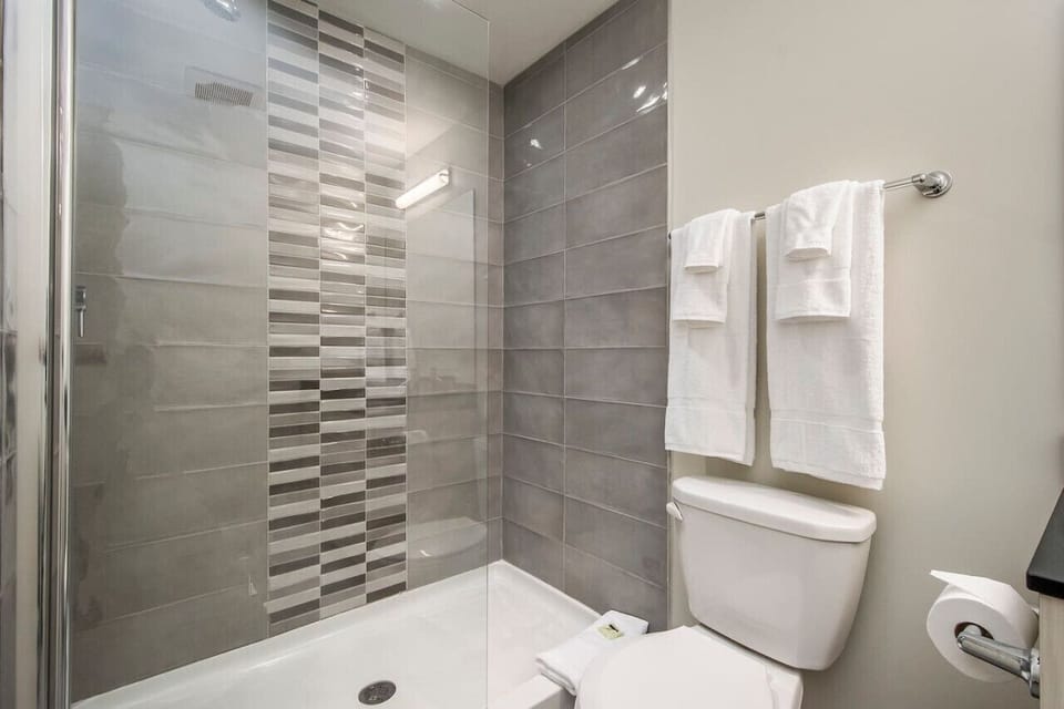 Features modern tile detailing, a spacious walk-in shower with glass enclosure, and plush, fresh white towels.