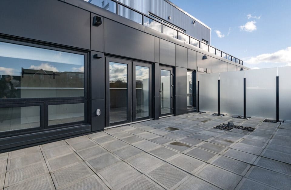`Spacious modern rooftop terrace featuring paved stone tiles, frosted glass privacy dividers, and floor-to-ceiling glass doors.`