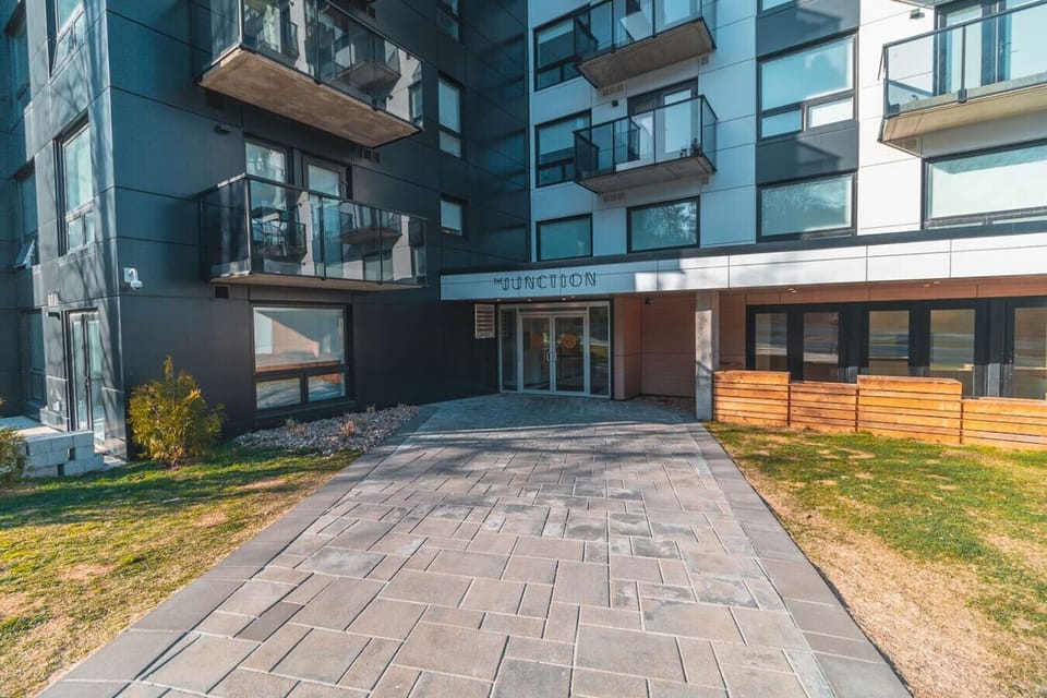 `Sleek and modern entrance to The Junction building, featuring a paved walkway, glass entry doors, and stylish architectural detailing.`