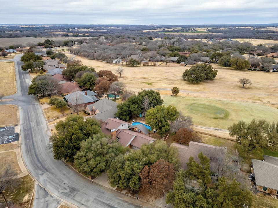 Drone view showcasing the home’s spacious layout, lush backyard, and prime location near the golf course