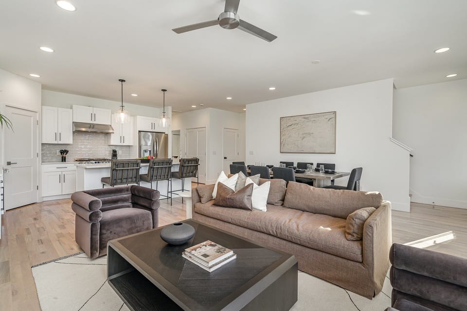 Relax in the cozy living room with ample seating, a flat-screen TV, and natural light pouring through large windows.